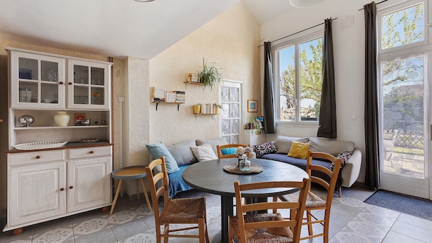A dining area with a round table, chairs, a cabinet with glass doors, a sofa, and a window with curtains.