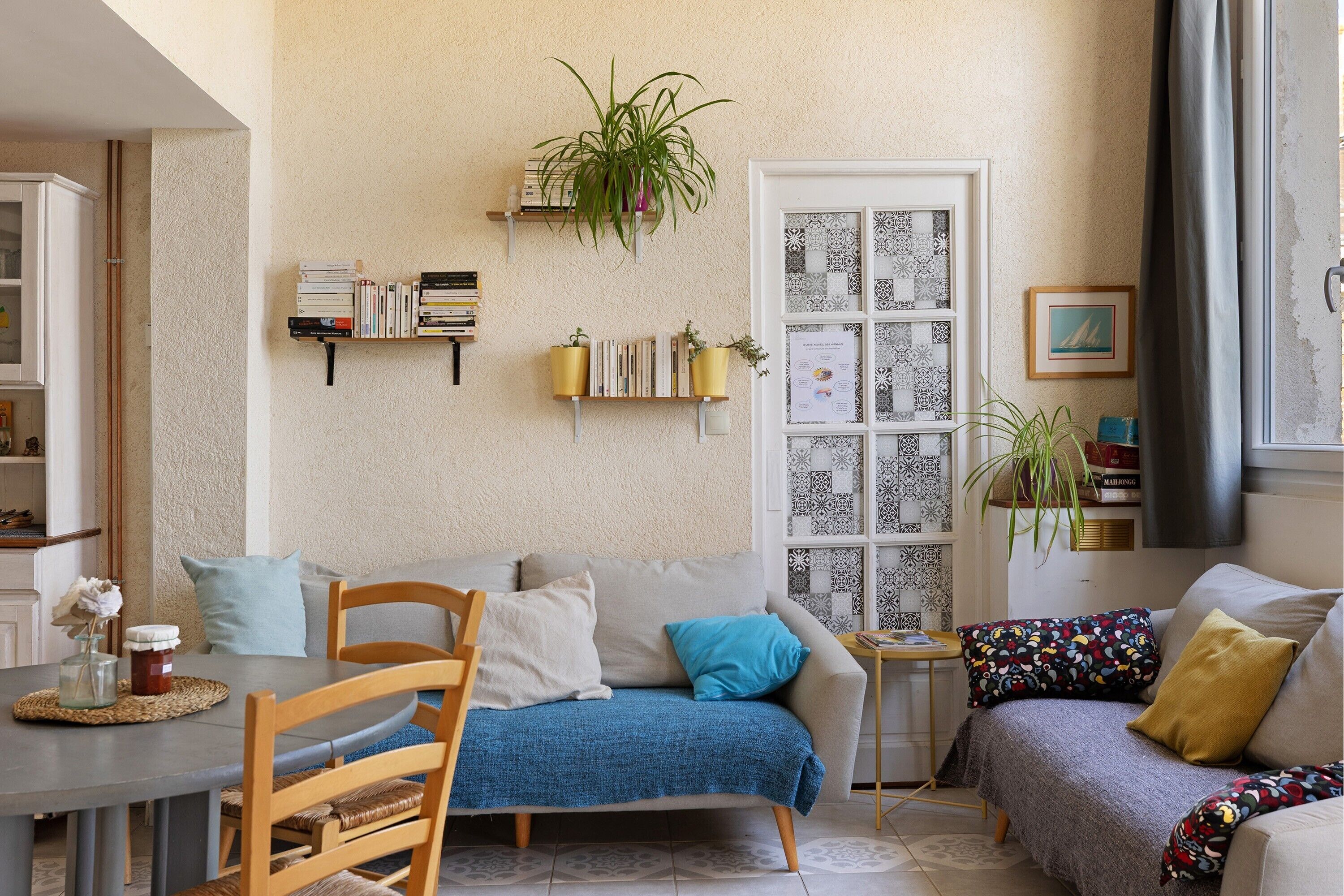 Una sala de estar con sofá, mesa de comedor, sillas, estantería y una ventana con cortinas estampadas.