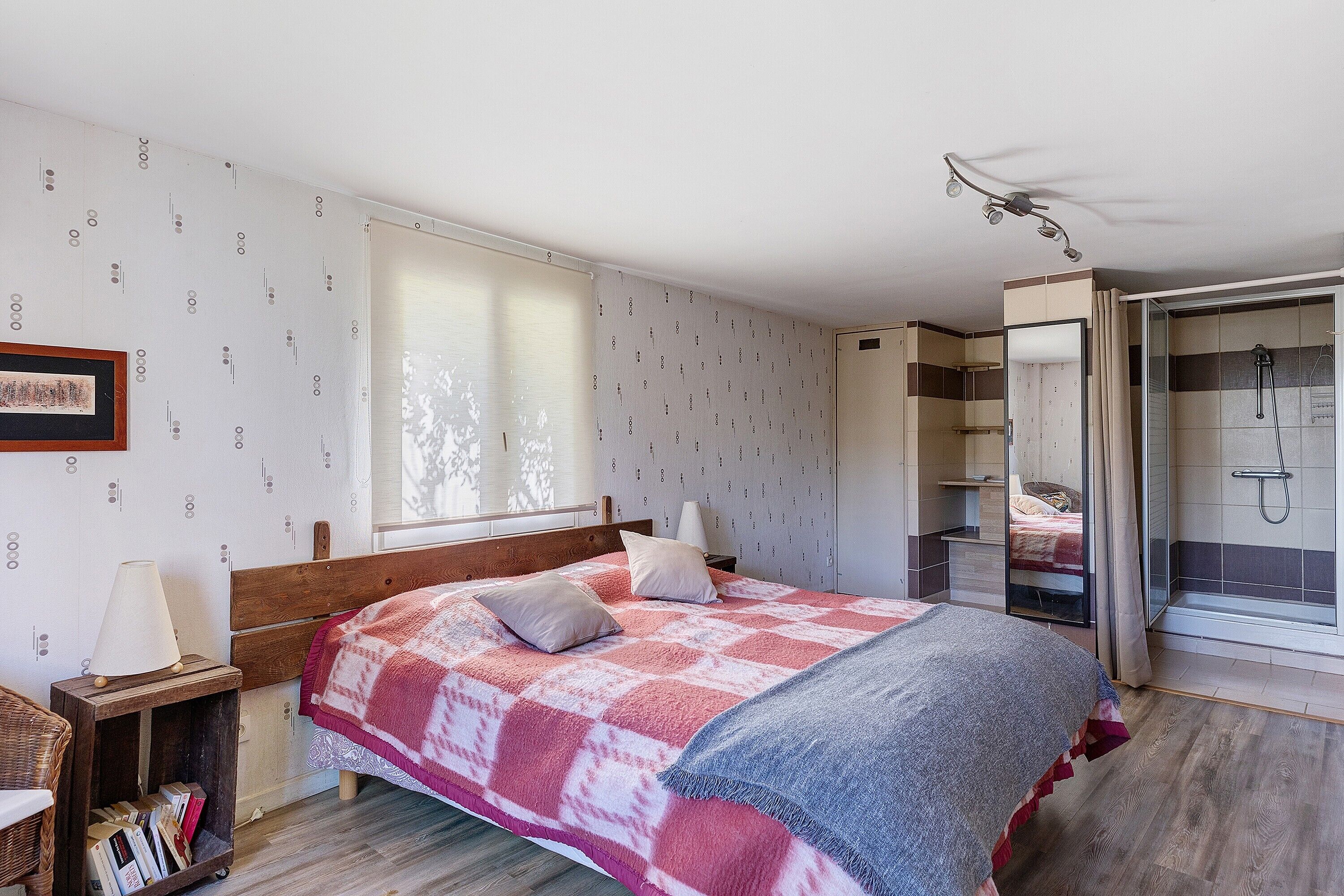 Ein Schlafzimmer mit Bett, Nachttisch, Lampe und Blick auf einen Duschbereich.