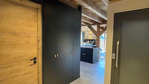 Un pasillo con techos de madera, una puerta oscura y una zona de cocina al fondo.