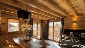 Un comedor amplio con una mesa y sillas de madera, un lámpara colgante y vistas al exterior a través de amplios ventanales.