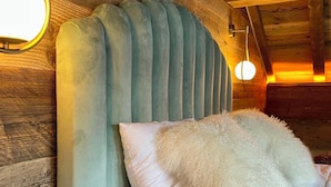 Interior de una cabaña de madera con una cama y un cabecero acolchado y almohadas mullidas.