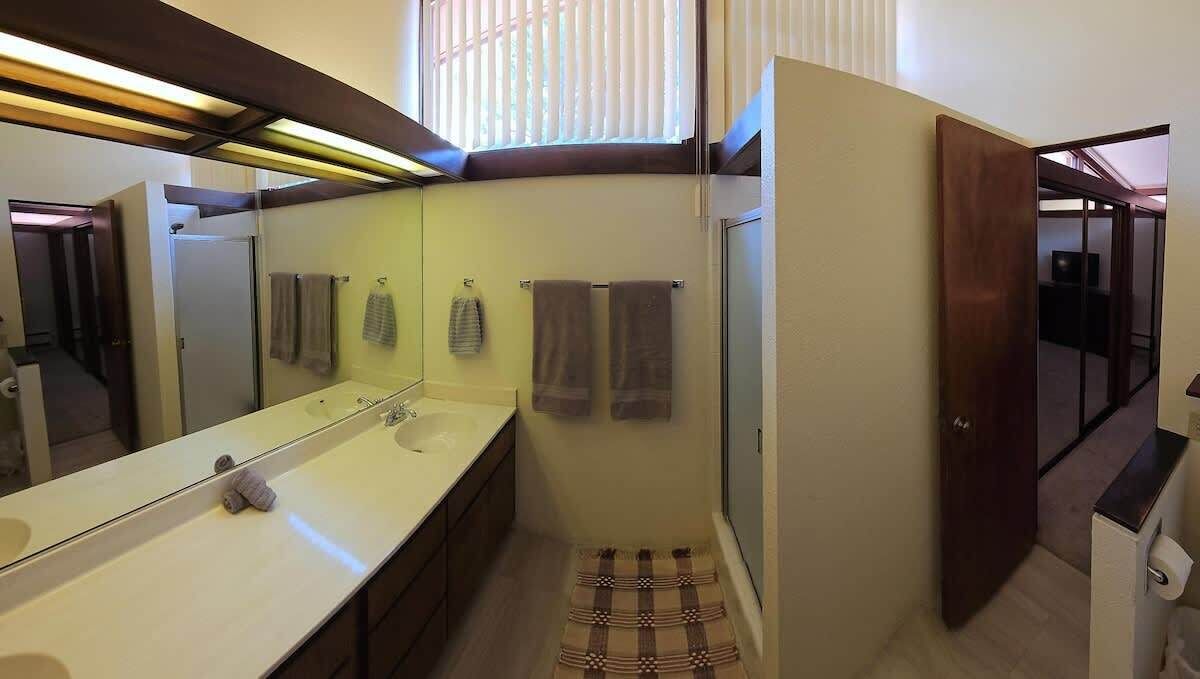A bathroom with a large mirror, two sinks, a towel rack, and a shower area.
