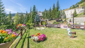 A garden with flower beds, a wooden swing, and a playground. - Grange Studio (Sauze di Cesana)