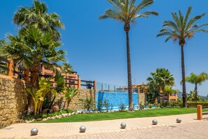 Ein Resort mit Palmen, einer Steinmauer, einem Pool mit blauem Mosaik und einem gepflasterten Weg.