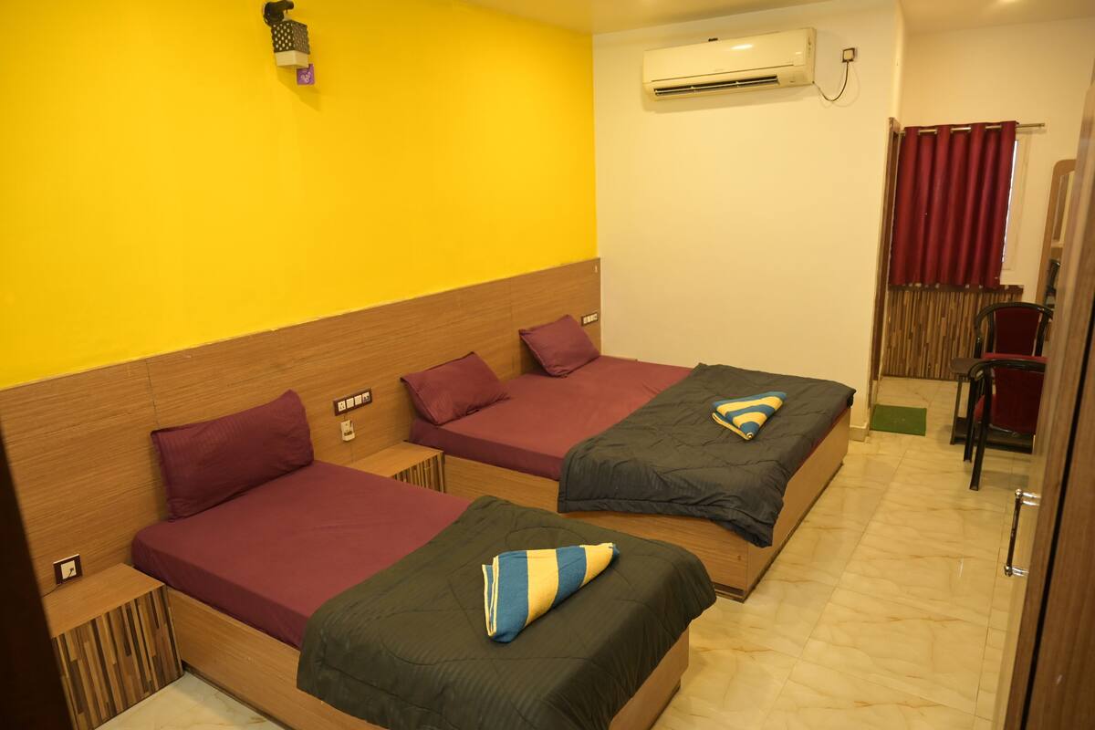 A hotel room with two beds, a wooden headboard, a yellow wall, an air conditioning unit, and a red curtain.