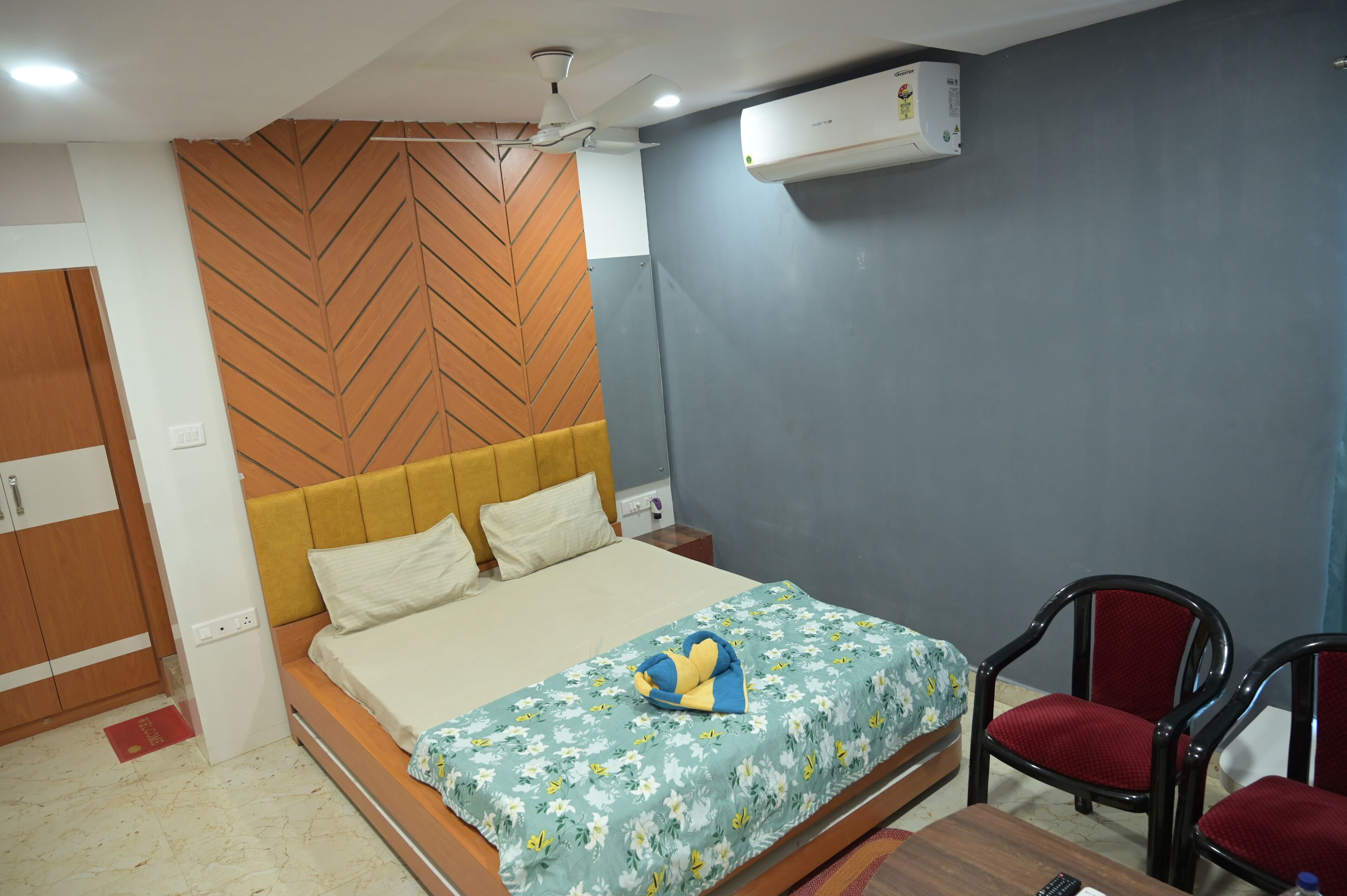 Un lit bien fait, avec une couvre-lit à motifs floraux, une tête de lit en bois et un climatiseur fixé au mur.