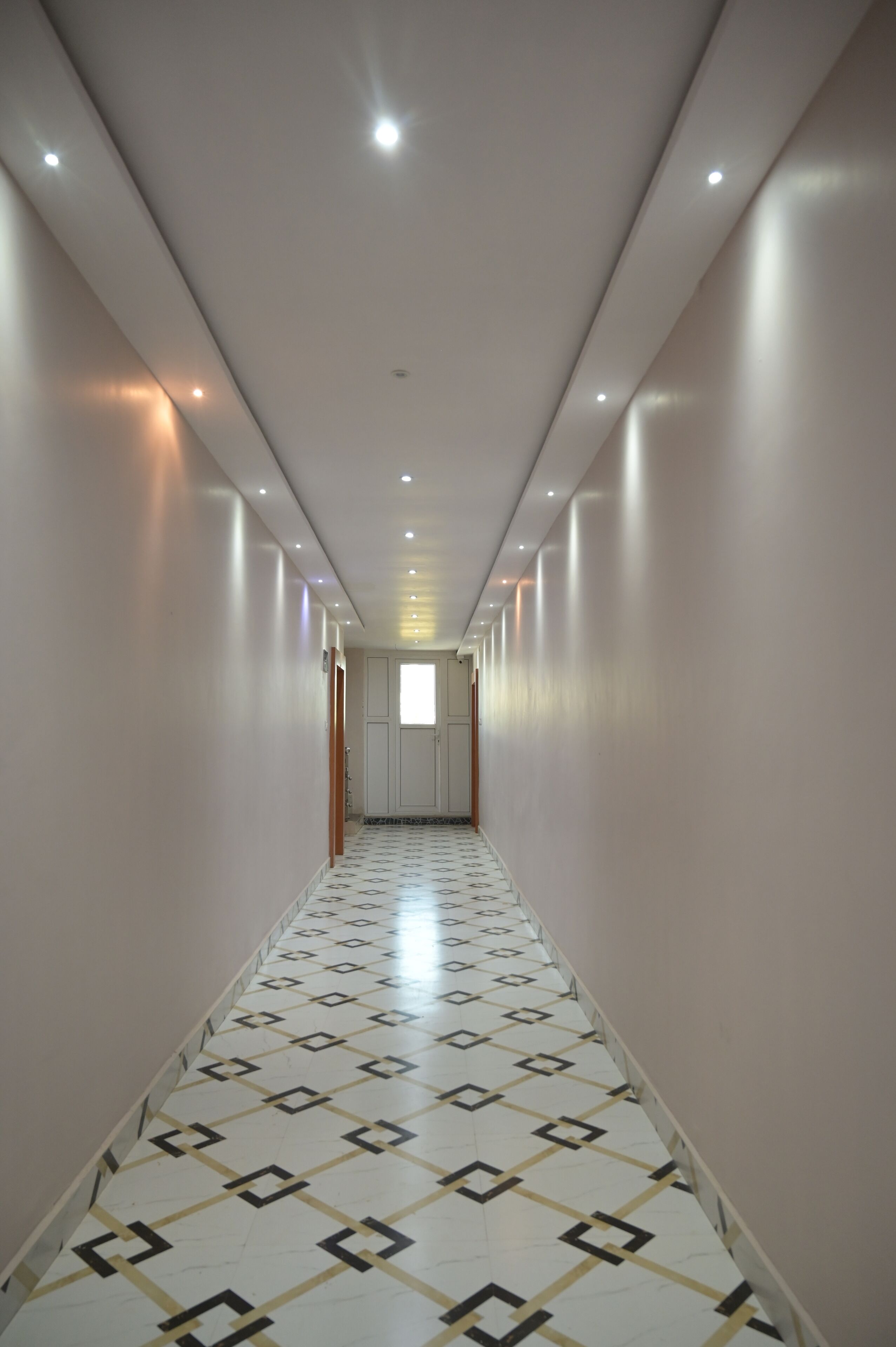 A long, narrow hallway with patterned flooring and recessed lighting.