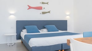 A bed with a blue headboard, two blue pillows, and a white bedspread. There are two wall-mounted lights and two fish-shaped wall decorations. - A welcoming space, ideal for two people (with the option of adding an infant), perfect for those seeking comfort and practicality. The bedroom offers a double bed—or comfortable single beds, depending on your needs—along with a small table and chairs (Porto San Paolo)