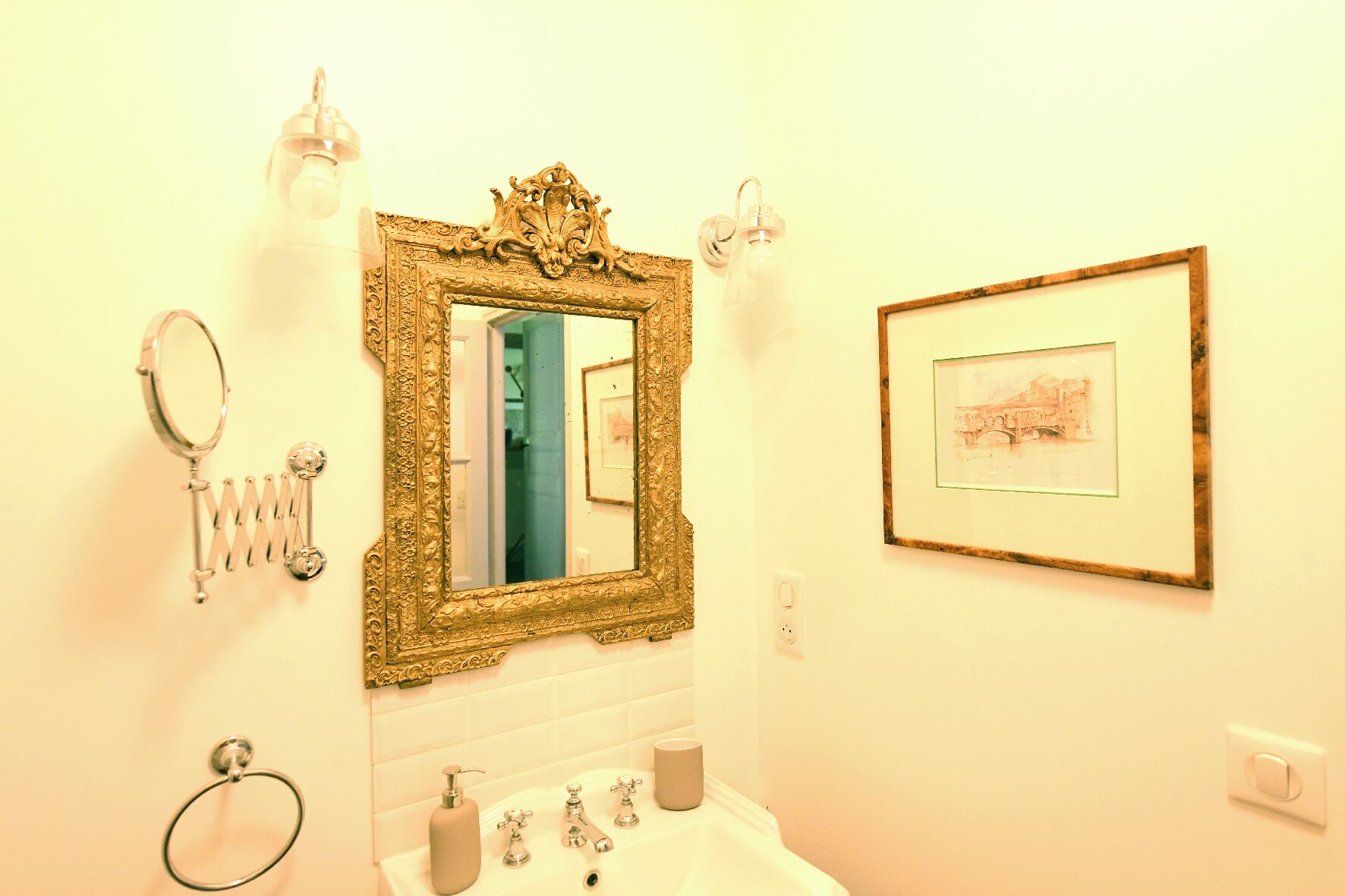 Un baño con un espejo grande y ornamentado, un cuadro en la pared y un lavamanos con un tozalete.