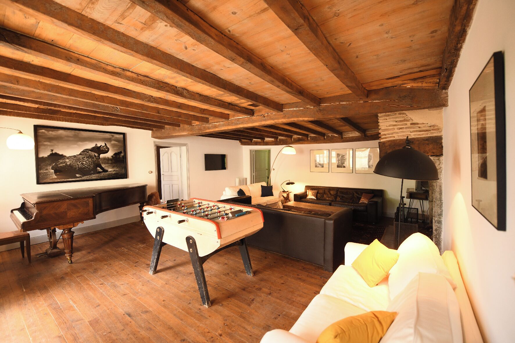 A cozy room with a wooden ceiling, a foosball table, a piano, a sofa, and a framed picture on the wall.
