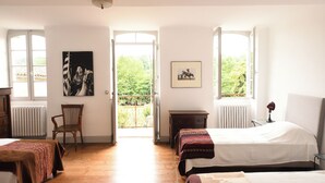 Ein Zimmer mit zwei Betten, einem Sessel, einem Heizkörper und einem Fenster mit Blick auf Grünflächen.