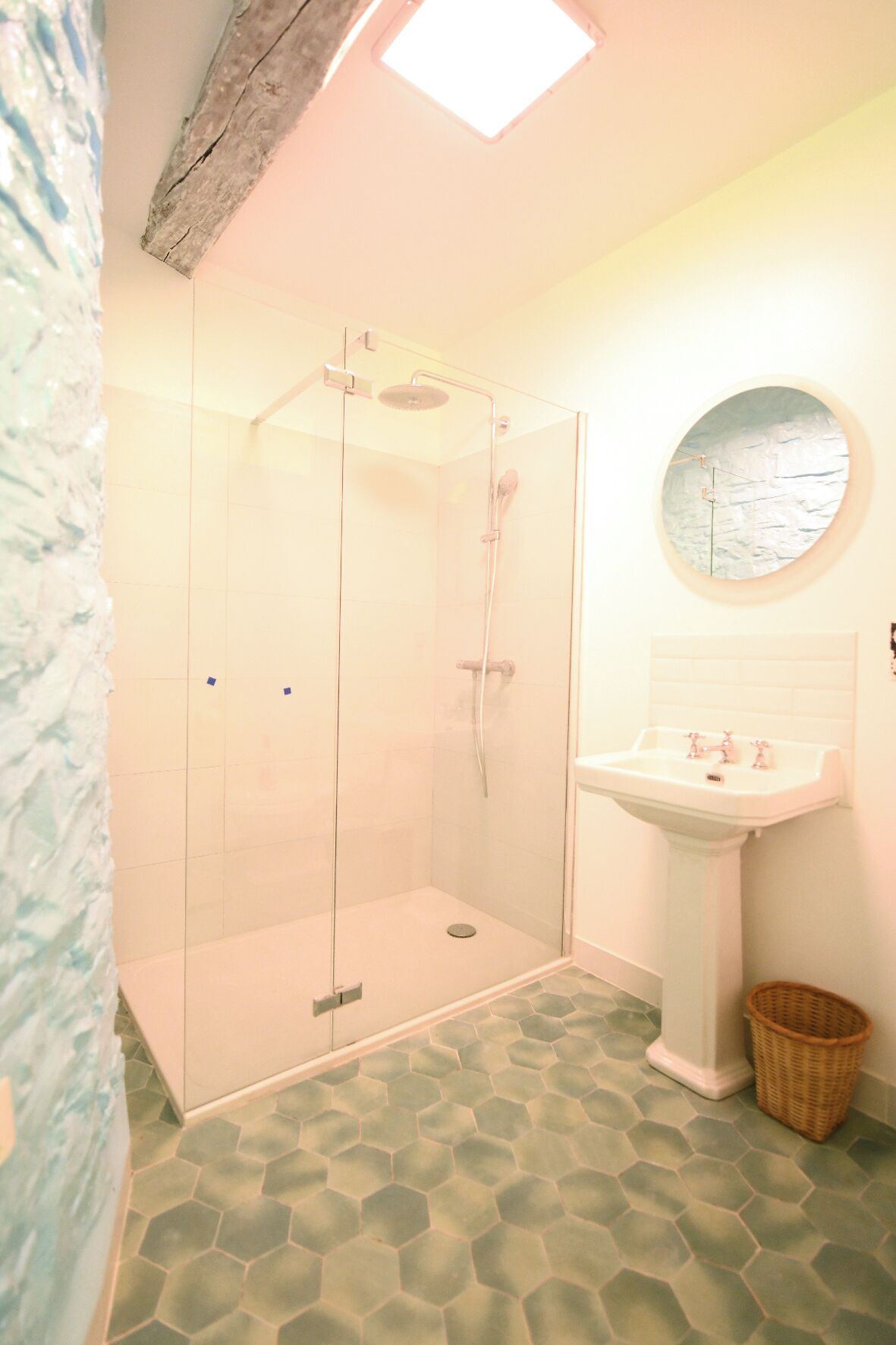A bathroom with a glass-enclosed shower, a round mirror, and a sink.