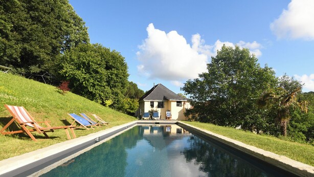 Ein Swimmingpool mit Liegestühlen, ein Haus im Hintergrund und umliegendes Grün.