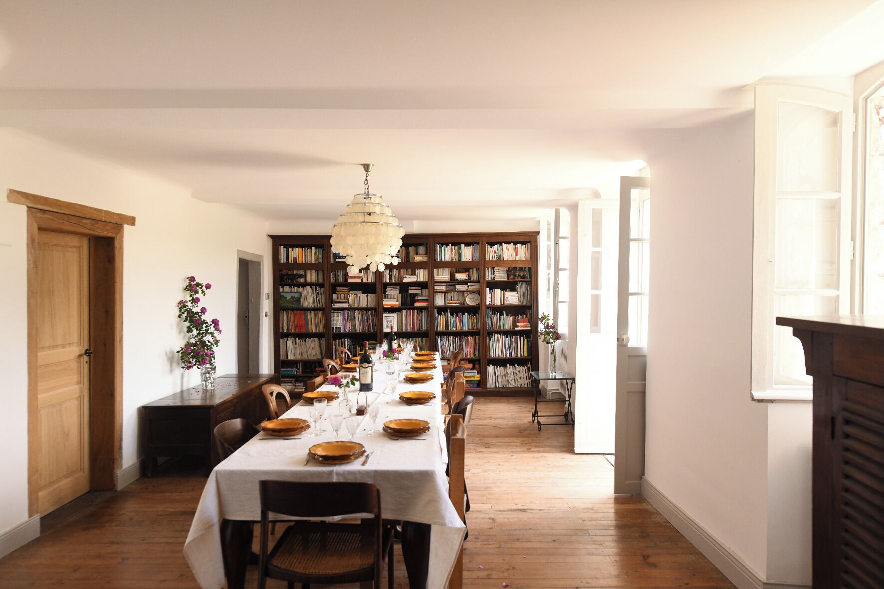 A dining room with a long table set for a meal, flanked by bookshelves filled with books.