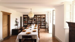 Ein Esszimmer mit einem langen Tisch, der für eine Mahlzeit gedeckt ist, und flankiert von Bücherregalen voller Bücher.