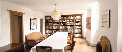 A dining room with a long table, chairs, a chandelier, and bookshelves filled with books.