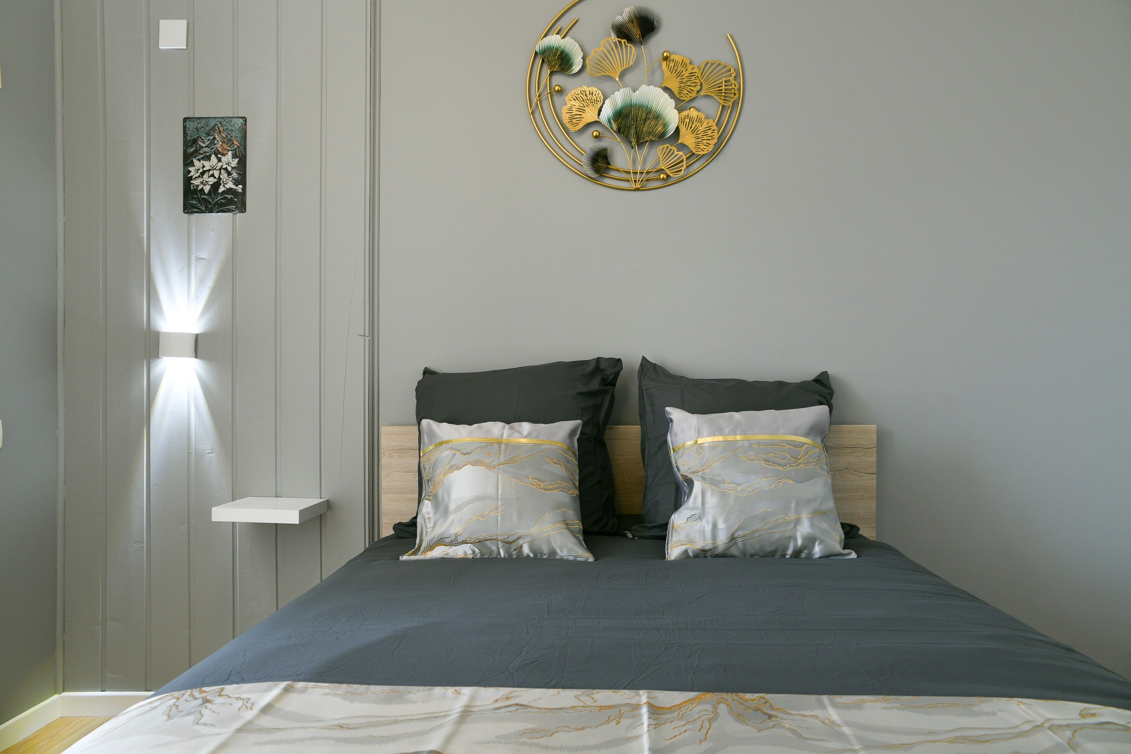 Une chambre à coucher avec un lit, des oreillers, une lampe fixée au mur et un élément décoratif mural.