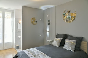 A bedroom with a bed, pillows, a wall-mounted artwork, a bedside table, and a door leading to a bathroom.