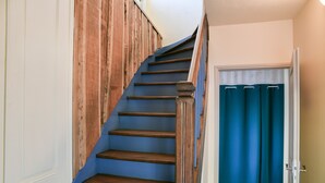 Un escalier avec des marches en bois et une rampe bleue, menant à une pièce dotée d’une porte et d’un rideau.