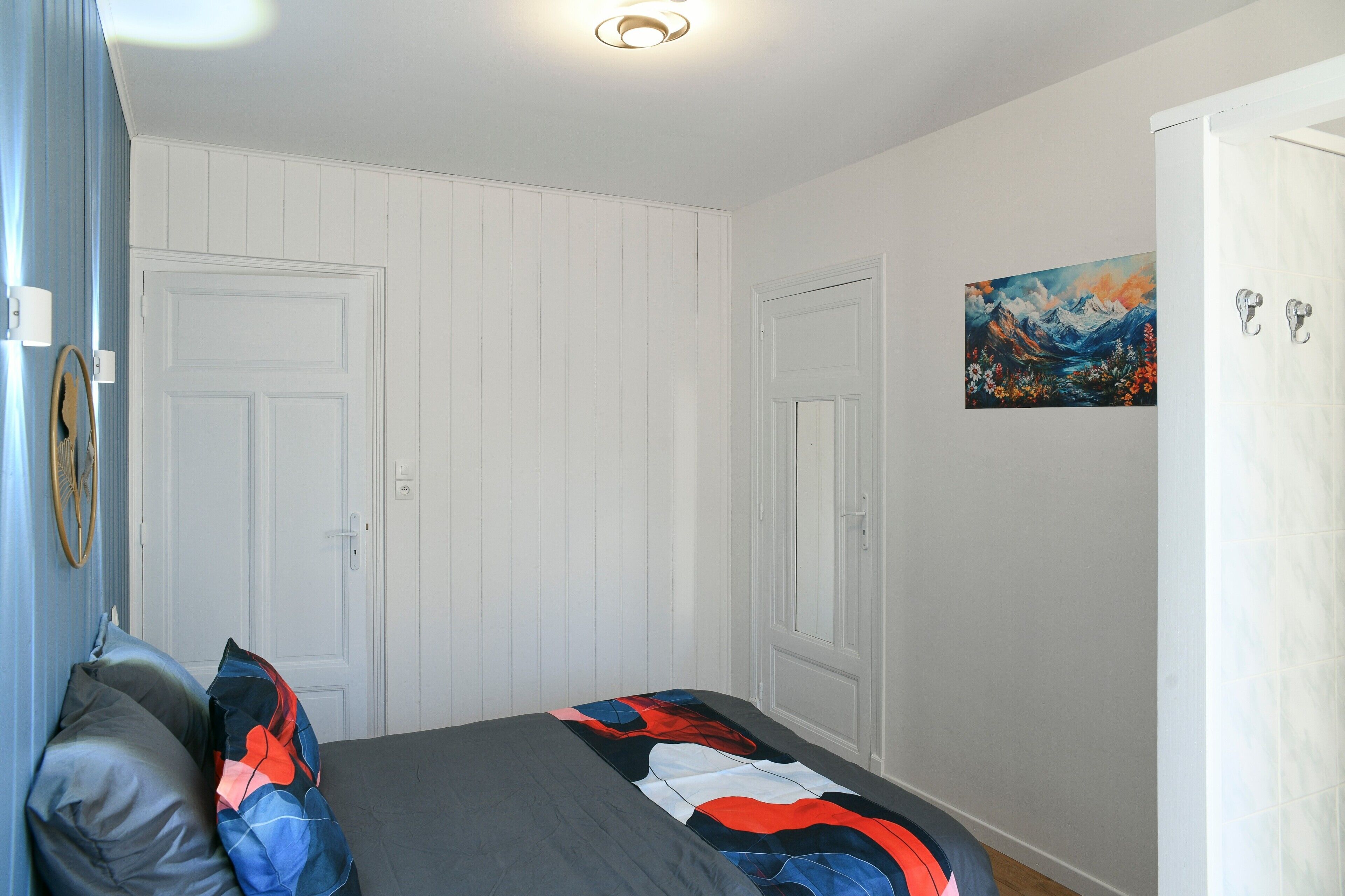 Ein Schlafzimmer mit einem Bett, zwei Türen, einem Gemälde und einem Spiegel.