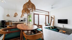 Una sala moderna con una mesa de comedor de madera, sillas con cojines verdes y una gran lámpara de fibra.