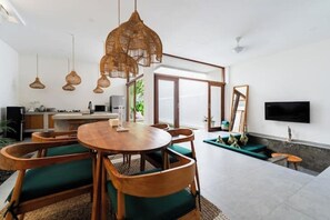 Ett modernt vardagsrum med ett matbord i trä, gröna stolar med vaddering och en stor, vävd lampa.