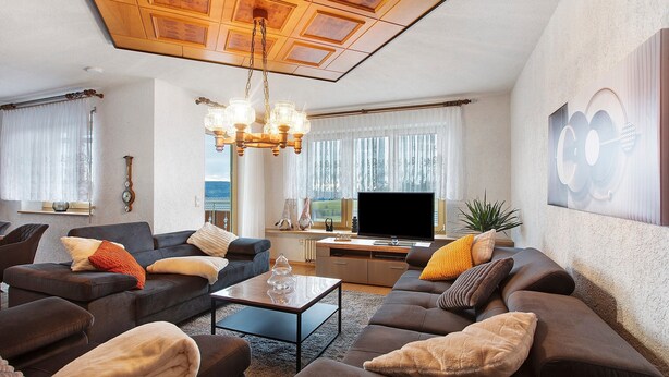A modern living room with a sofa set, a coffee table, a TV, and a chandelier. - Alpine View Apartment with Mountain Views, Balcony & Wi-Fi (Schopfheim)