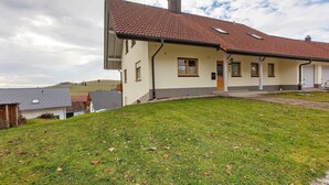 A two-story house with a red-tiled roof, a front porch, and a small front yard. - Alpine View Apartment with Mountain Views, Balcony & Wi-Fi (Schopfheim)