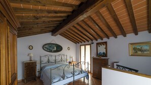Une chambre à coucher avec un lit, des poutres en bois au plafond, une commode, une table de chevet et un tableau au mur.