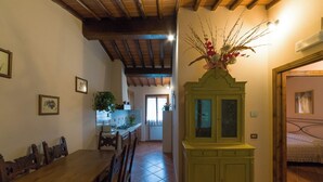 Un coin repas avec une table et des chaises en bois, un buffet vert aux portes vitrées, et une cuisine en arrière-plan.