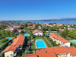A residential area with multiple houses, a large swimming pool, and a view of the sea. - MGH - Sirmione Lake & Pool (Sirmione)