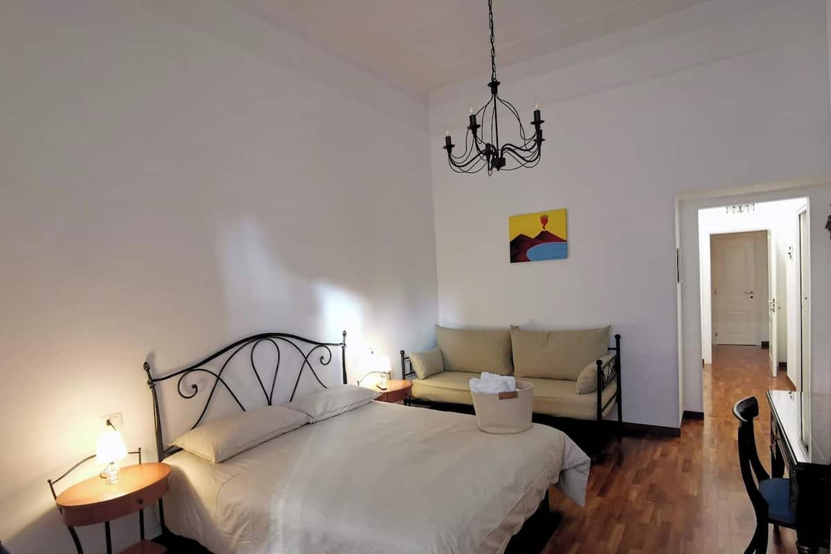 Una camera da letto con un letto, comodini, una lampada a sospensione, un divano e un quadro appeso al muro.
