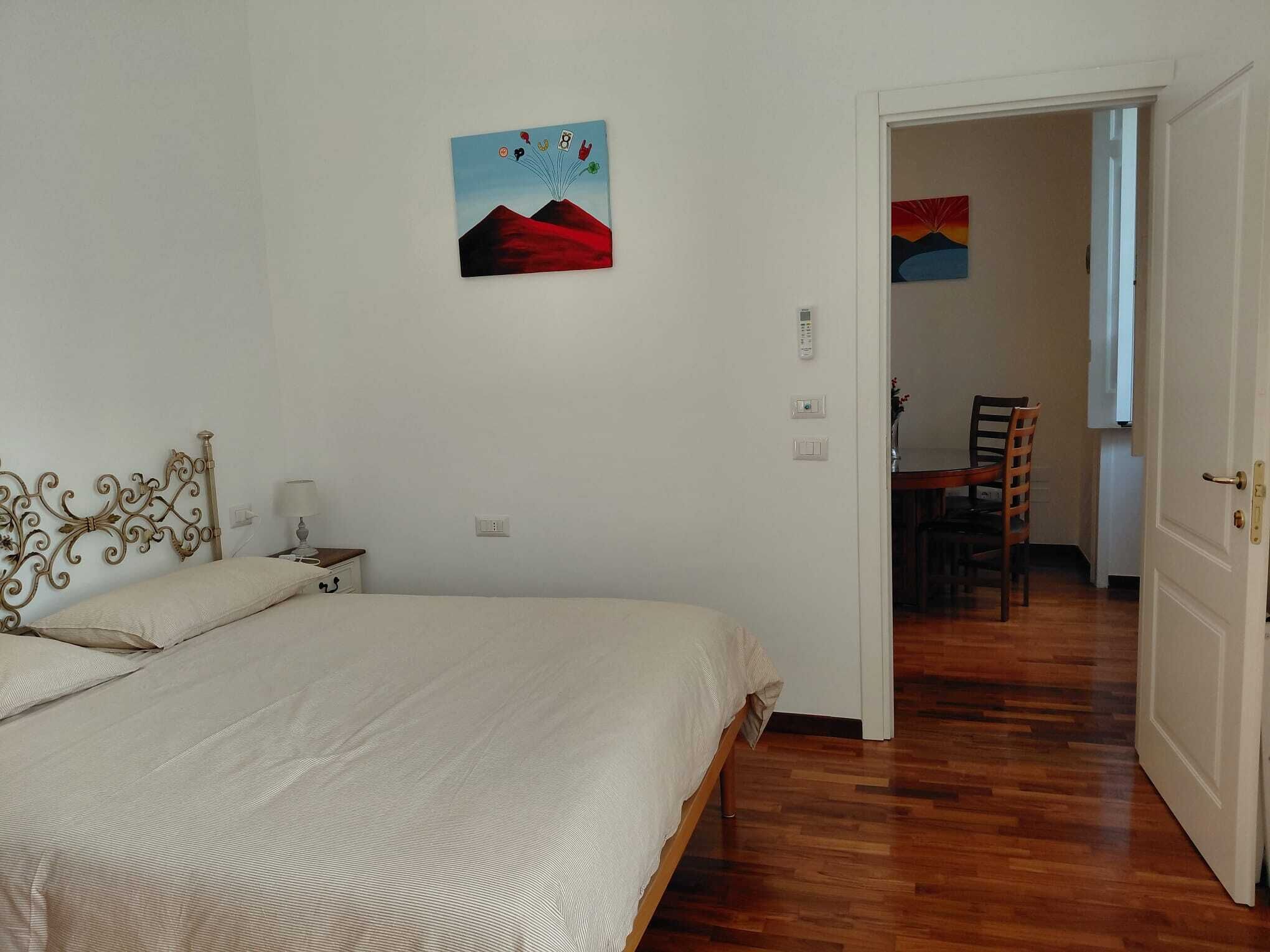 A bedroom with a bed, a nightstand, a lamp, and a painting on the wall.