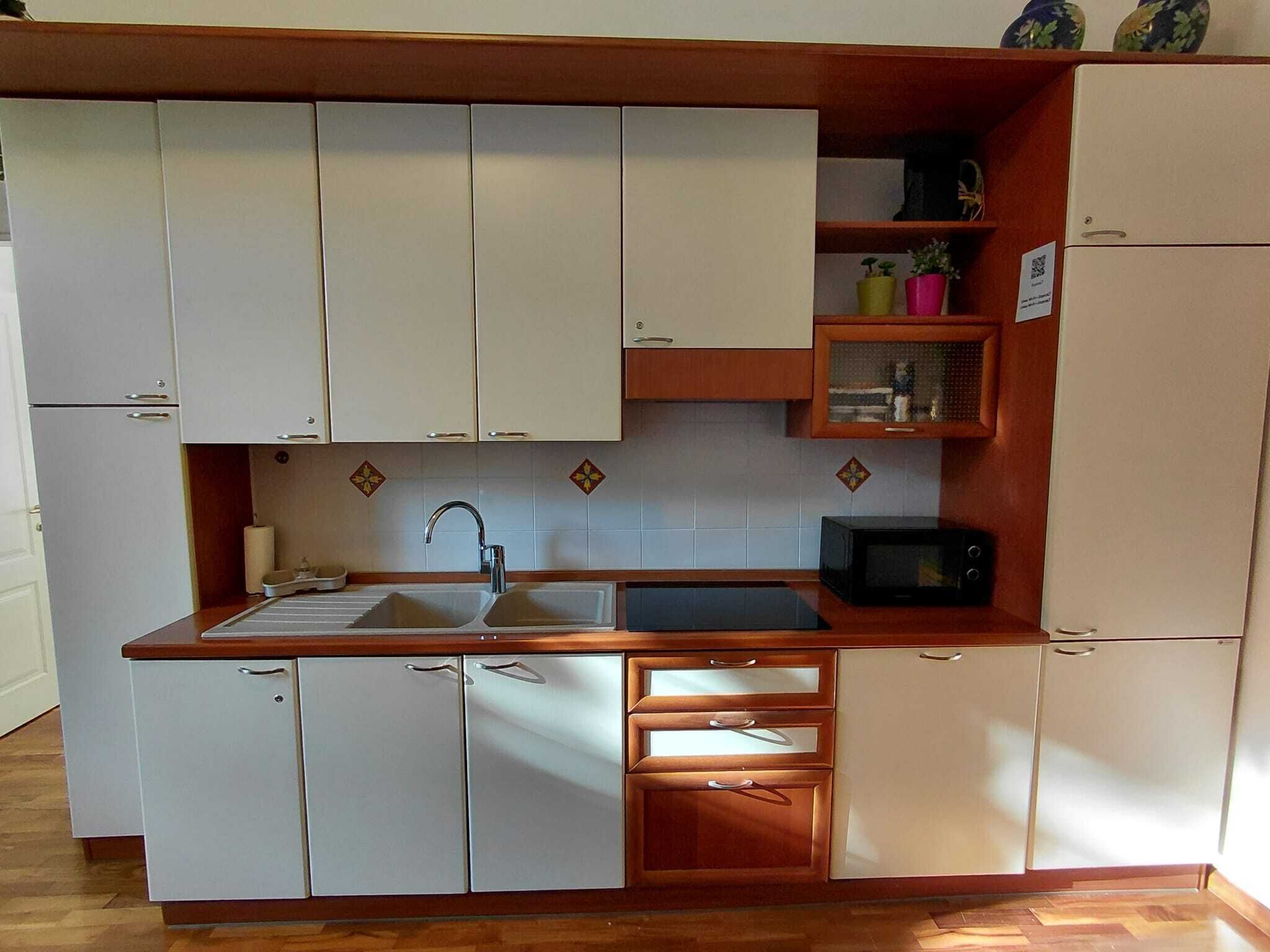 A compact kitchen with white cabinets, a sink, a microwave, and a small shelf with decorative items.