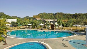 A large outdoor swimming pool with a no diving sign, surrounded by lounge chairs and umbrellas, with a building in the background. - The Corbett Hideaway - By Leisure Hotels (Ramnagar)
