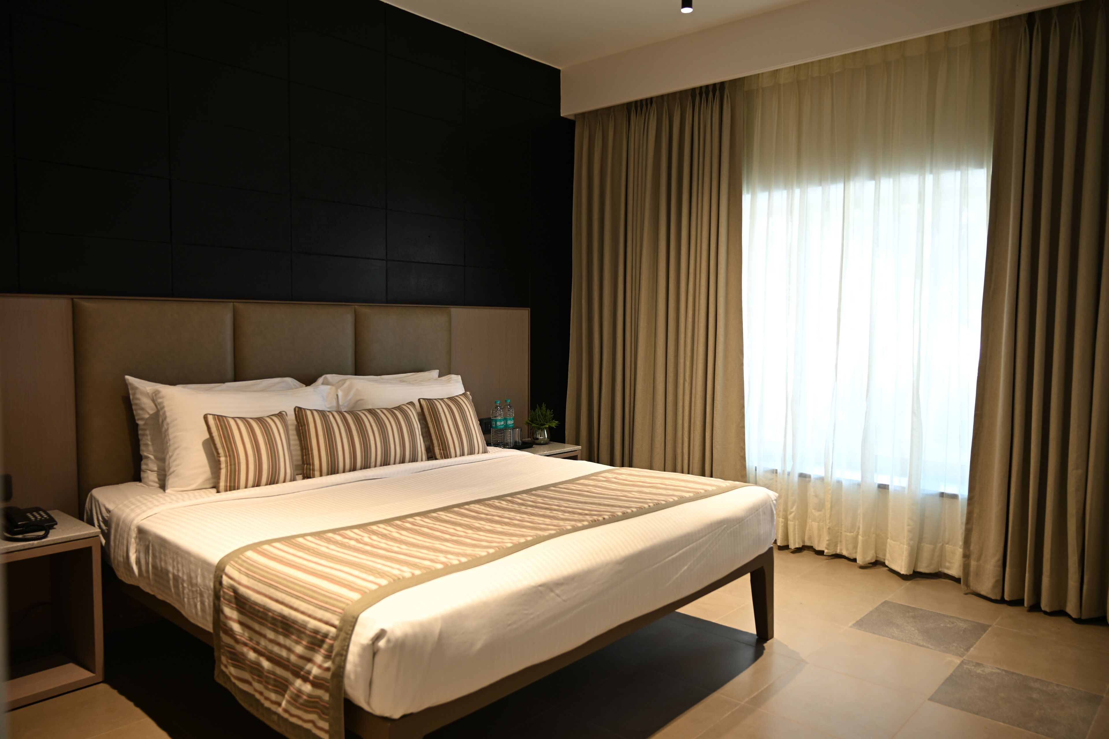 A hotel room with a large bed, a nightstand, a telephone, and a window with curtains.