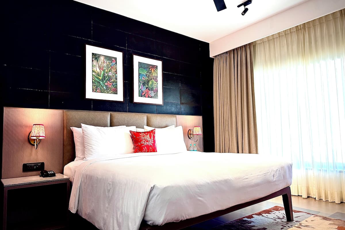 Ein modernes Hotelzimmer mit einem großen Bett, zwei Wandlampen, einem Telefon und gerahmten Kunstwerken über dem Bett.