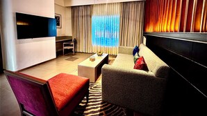 A modern living room with a sofa, armchair, coffee table, and a flat-screen TV mounted on the wall. - The Corbett Hideaway - By Leisure Hotels (Ramnagar)