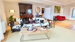 Een woonkamer met een bank met koeienprint, een salontafel, een kast en een rode fauteuil.