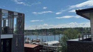 Een modern gebouw met een glazen gevel met uitzicht op een jachthaven met boten en een heldere lucht.