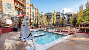 Une piscine avec un plongeoir et des chaises longues, entourée d’immeubles à plusieurs étages dotés de balcons et d’espaces de détente en plein air.