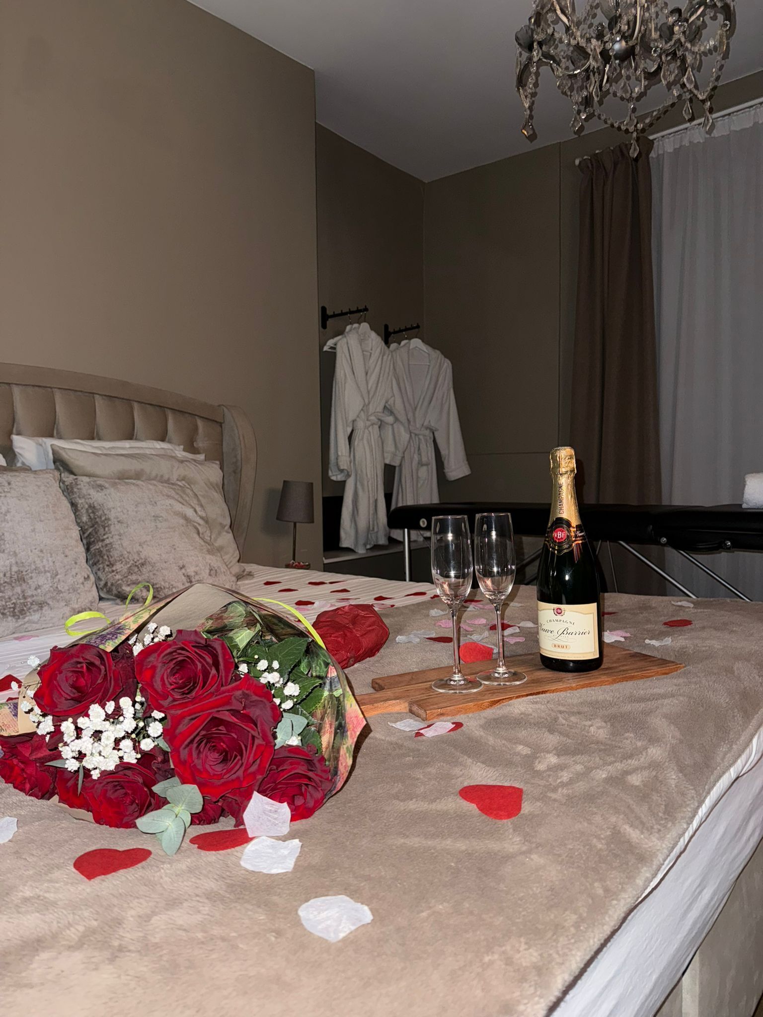 Ein Bett mit einem Rosenstrauß, zwei Champagnerflaschen und Gläsern auf einer mit Rosenblättern belegten Bettdecke.