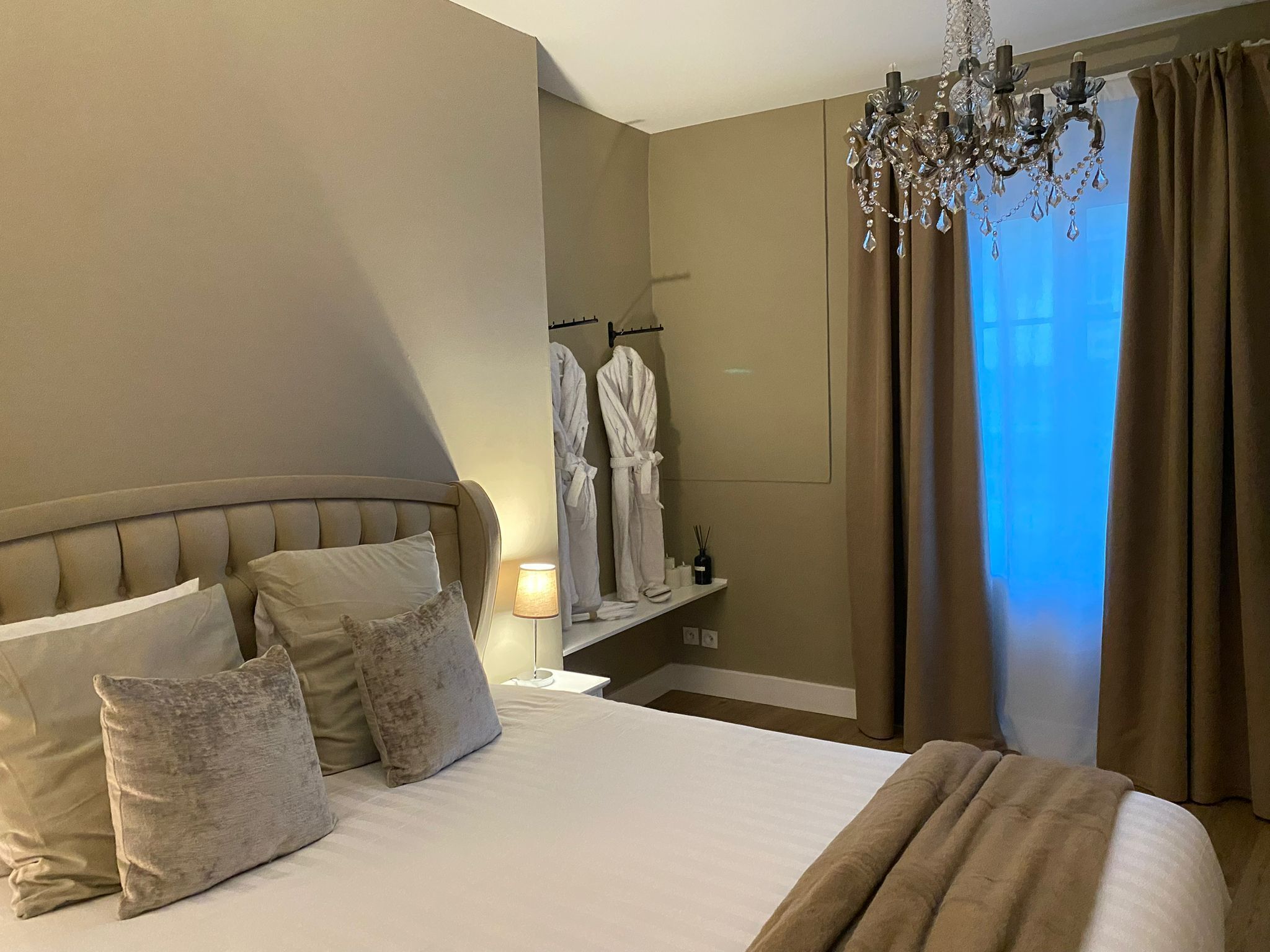 Ett hotellrum med en stor säng, en kristallkrona och utsikt över omgivningarna genom fönstret.