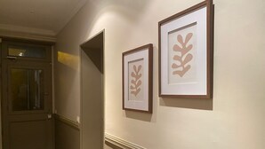 Un couloir avec des œuvres d’art encadrées accrochées au mur, une porte et un radiateur.