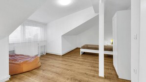A modern, white-walled room with a sloped ceiling, a wooden floor, and a bed with a brown cover. - Spacious Renovated House in Wolfsthal, Austria - Perfect for Families and Groups (Wolfsthal)