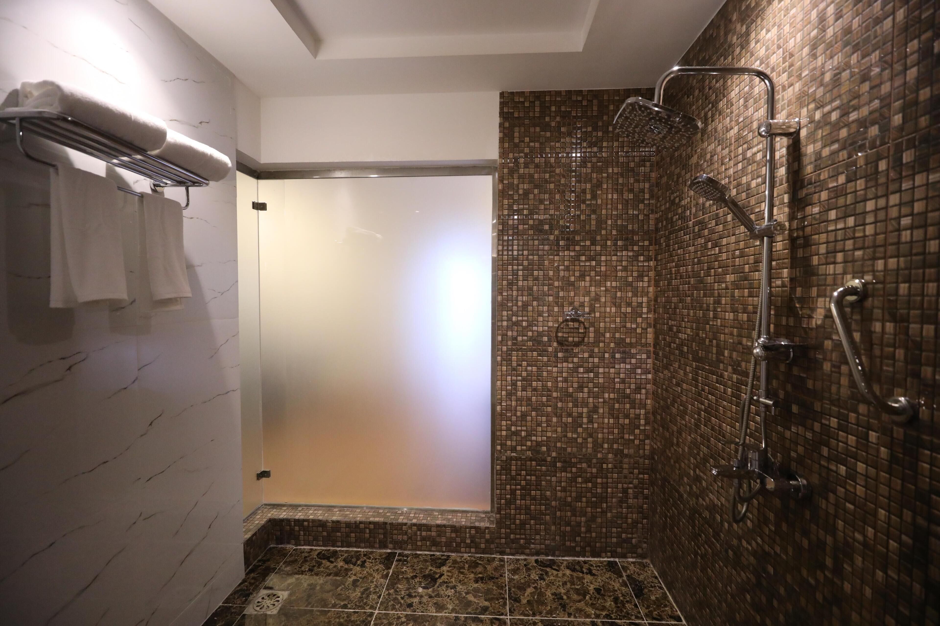 Een douche met betegelde wand, een handdoekrek met handdoeken en een deur naar een andere kamer.