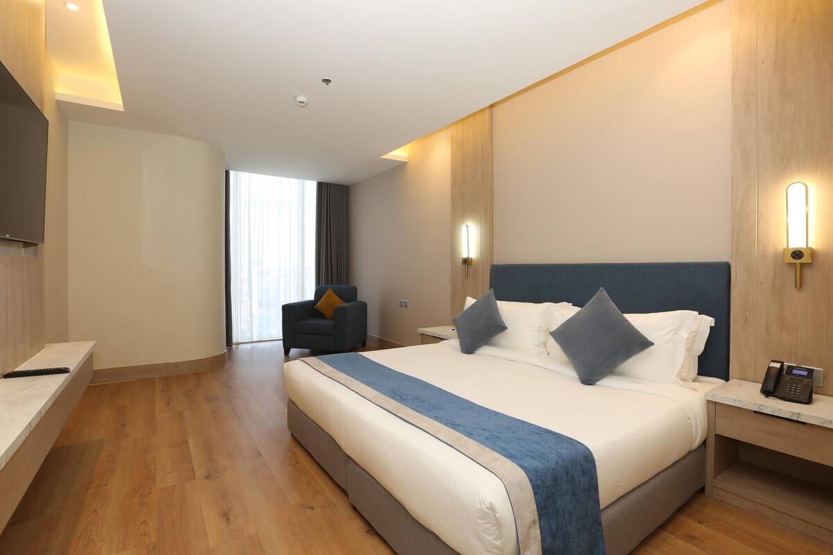 A hotel room with a large bed, bedside tables, a desk, a chair, and a TV.