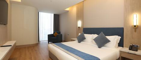 A hotel room with a large bed, bedside tables, a desk, a chair, and a TV.