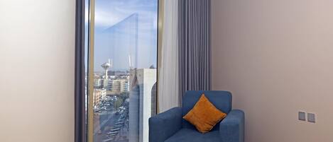 A modern room with a large window, a blue armchair with a cushion, and a view of a cityscape.